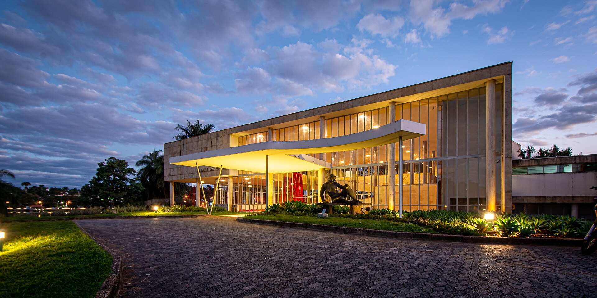 Fachada do Museu de Arte da Pampulha, antigo cassino projetado por Niemeyer, iluminada ao entardecer, com uma escultura em frente