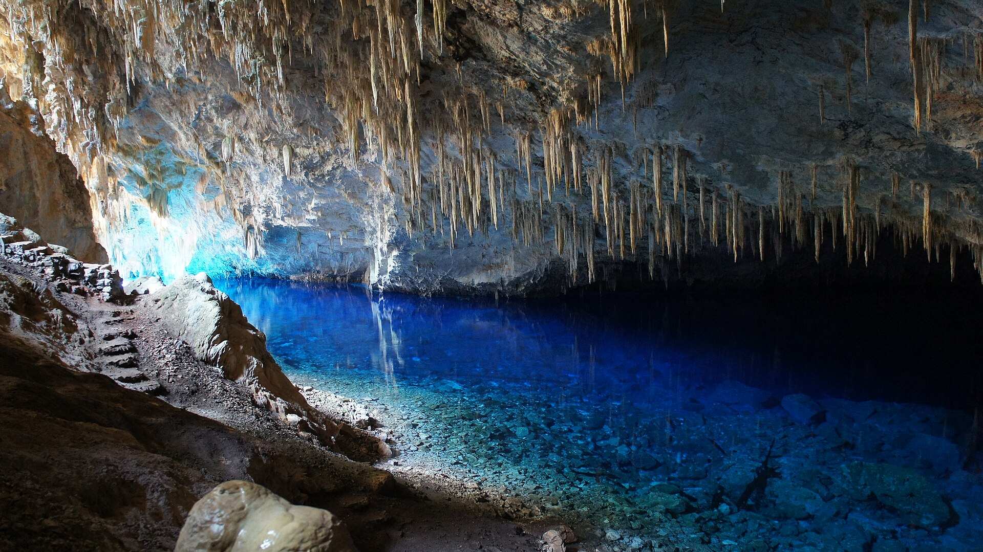 Lago de água azul-turquesa transparente dentro da Gruta do Lago Azul, com estalactites no teto da caverna