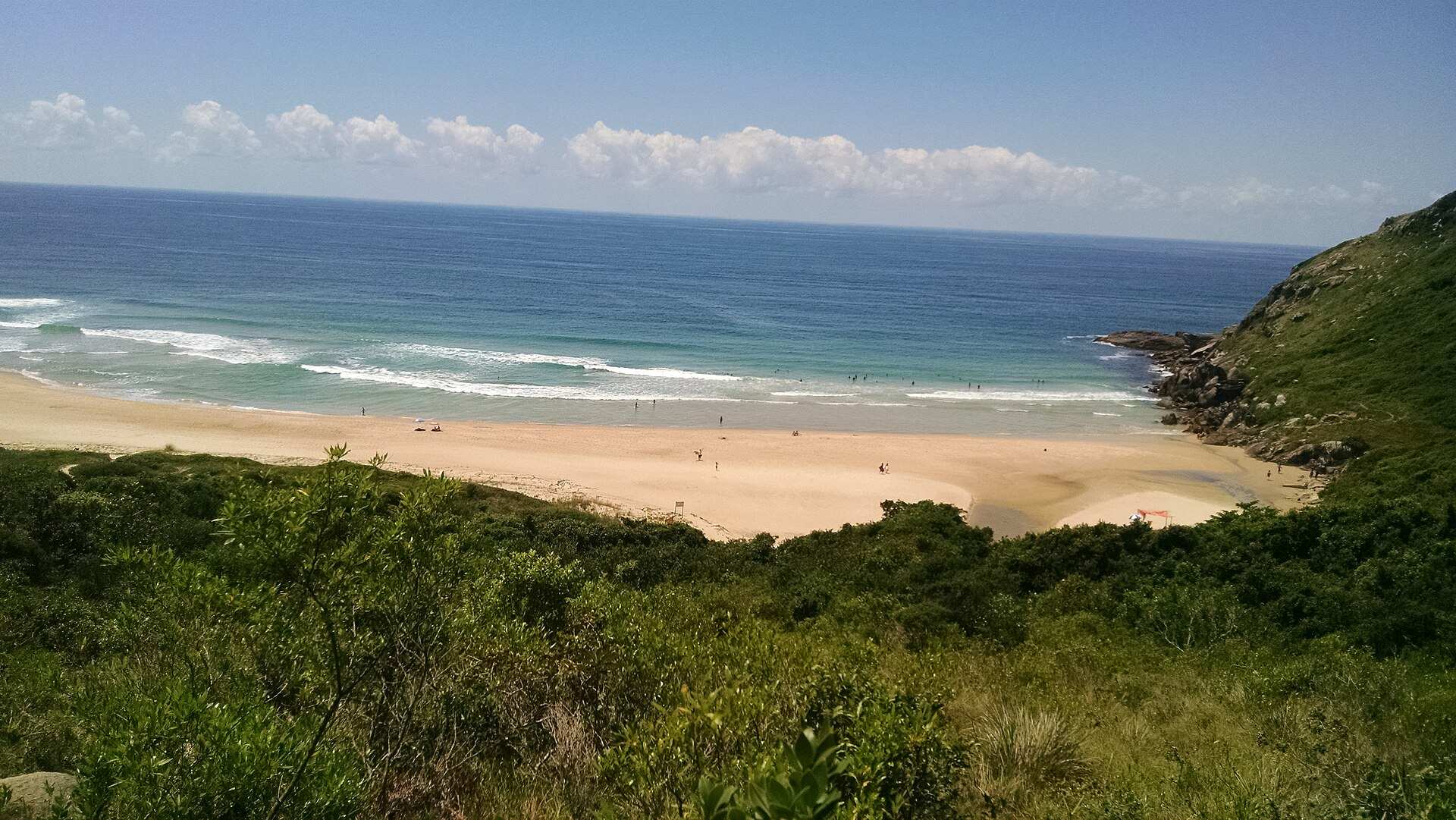 Praia da Lagoinha do Leste vista do alto, com faixa de areia clara, mar azul e vegetação de morro